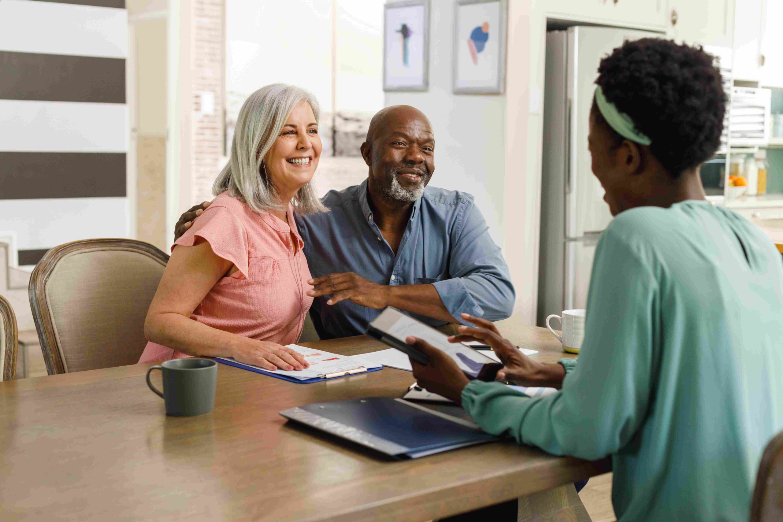 A smiling couple meeting with a consultant at a table with folders and coffee mugs