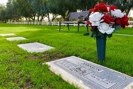 Flat lawn burial markers on green grass with a flower vase and a bench in the background