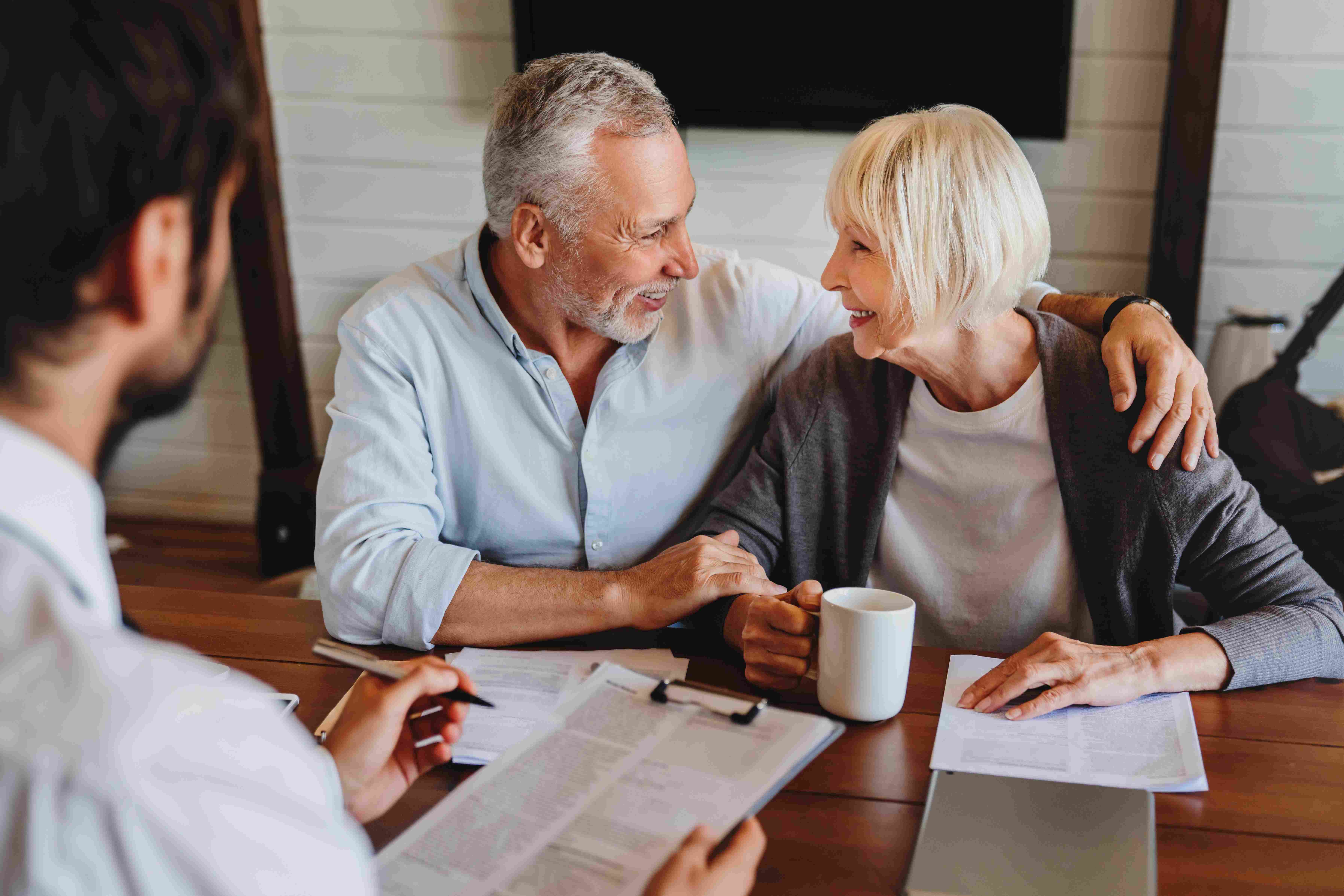 An older couple smiling at each other during a planning meeting with a consultant reviewing paperwork