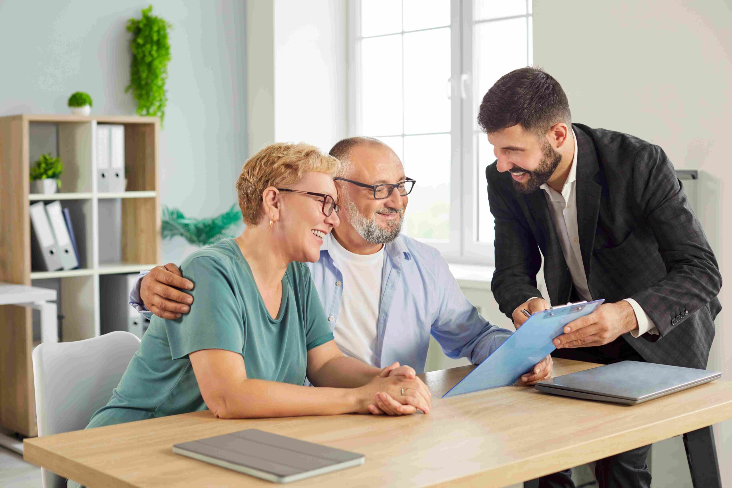 A couple sitting at a table reviewing a document with a consultant standing beside them